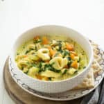 A bowl of chicken tortellini soup with carrots and spinach in a creamy broth.