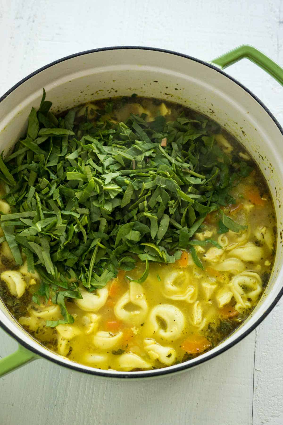 A soup pot with tortellini soup with spinach and heavy cream.