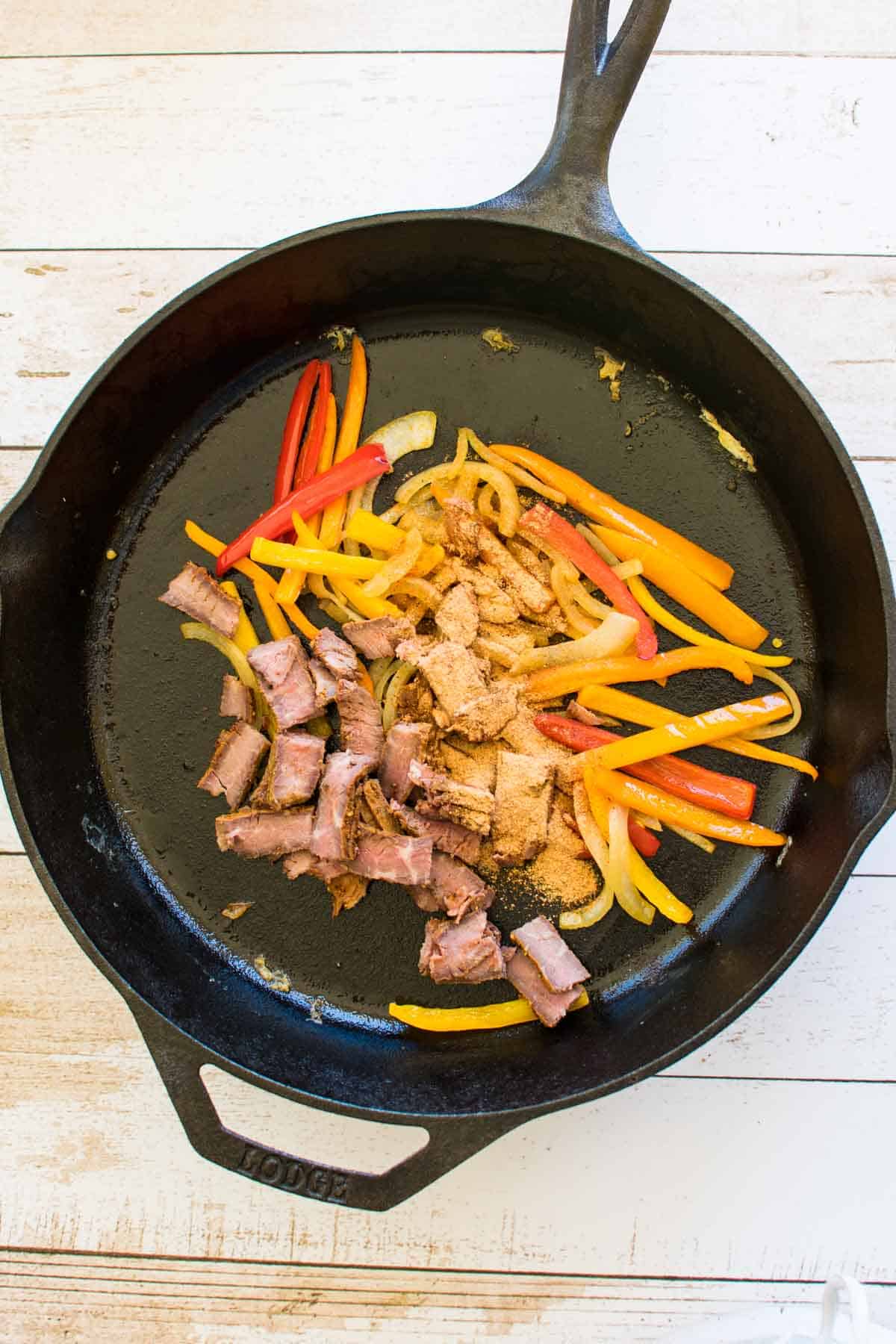 Sliced onions and peppers in a cast iron skillet.