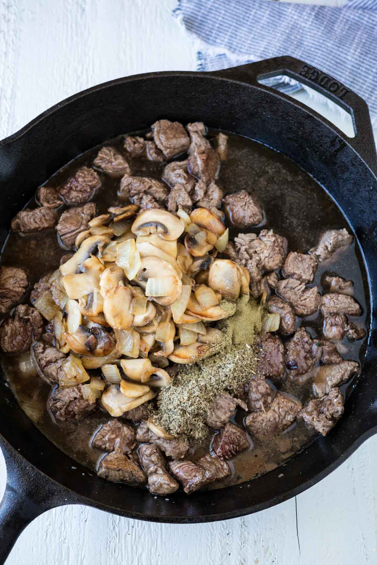 Mushrooms, onions, and steak bites in a cast iron skillet with gravy and herbs.