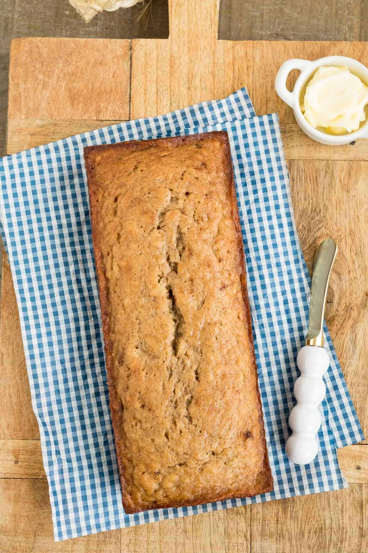 A loaf of banana bread with a dish of butter and a butter spreading knife.