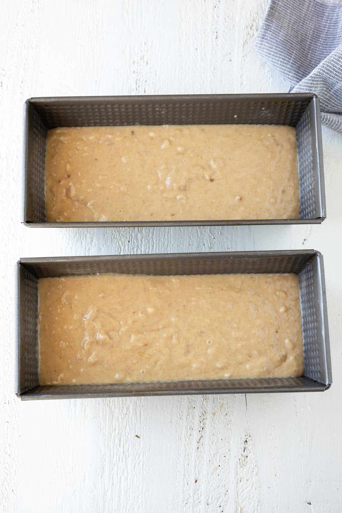 Two loaves of banana bread batter in bread pans.