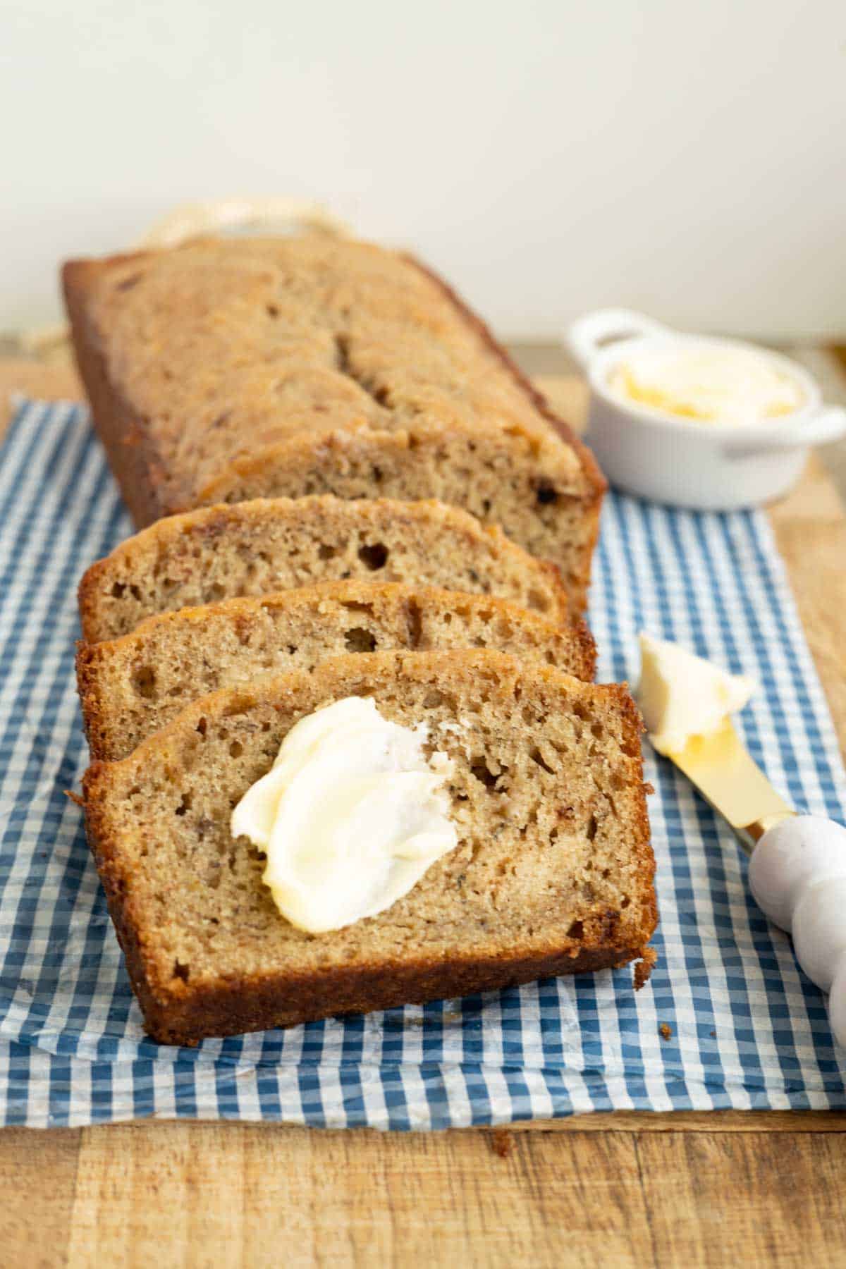 A loaf of banana bread with a few slices spread with butter.