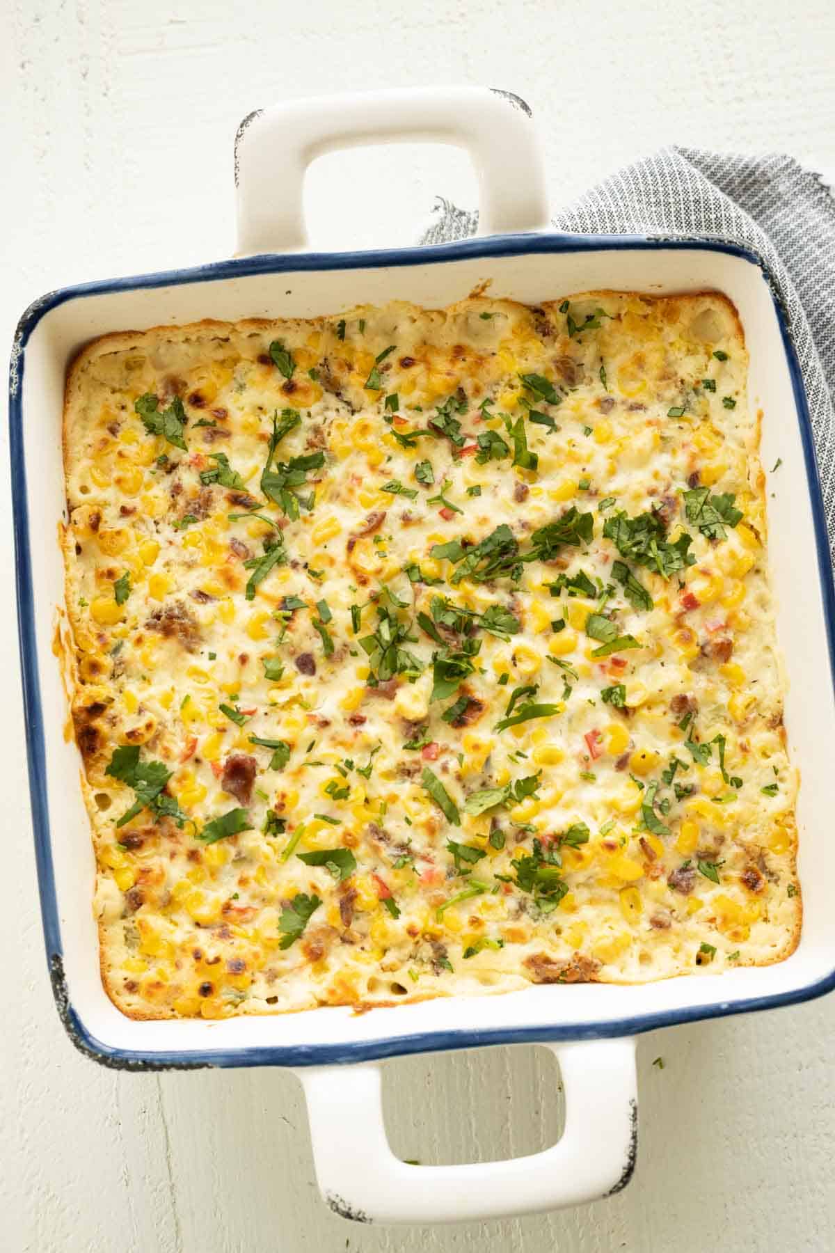 A hot cheesy corn dip sprinkled with cilantro in a white baking dish.