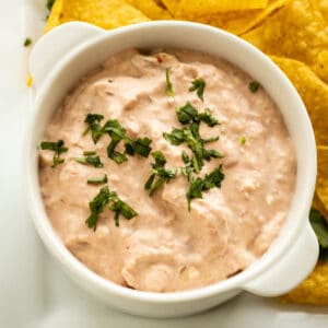 A white dish with creamy salsa dip sprinkled with cilantro dip with chips on the side.