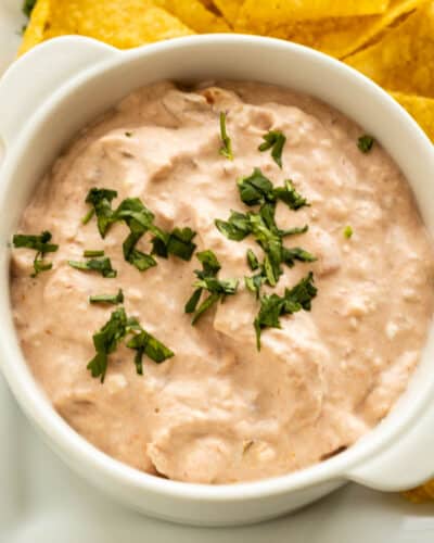 A white dish with creamy salsa dip sprinkled with cilantro dip with chips on the side.