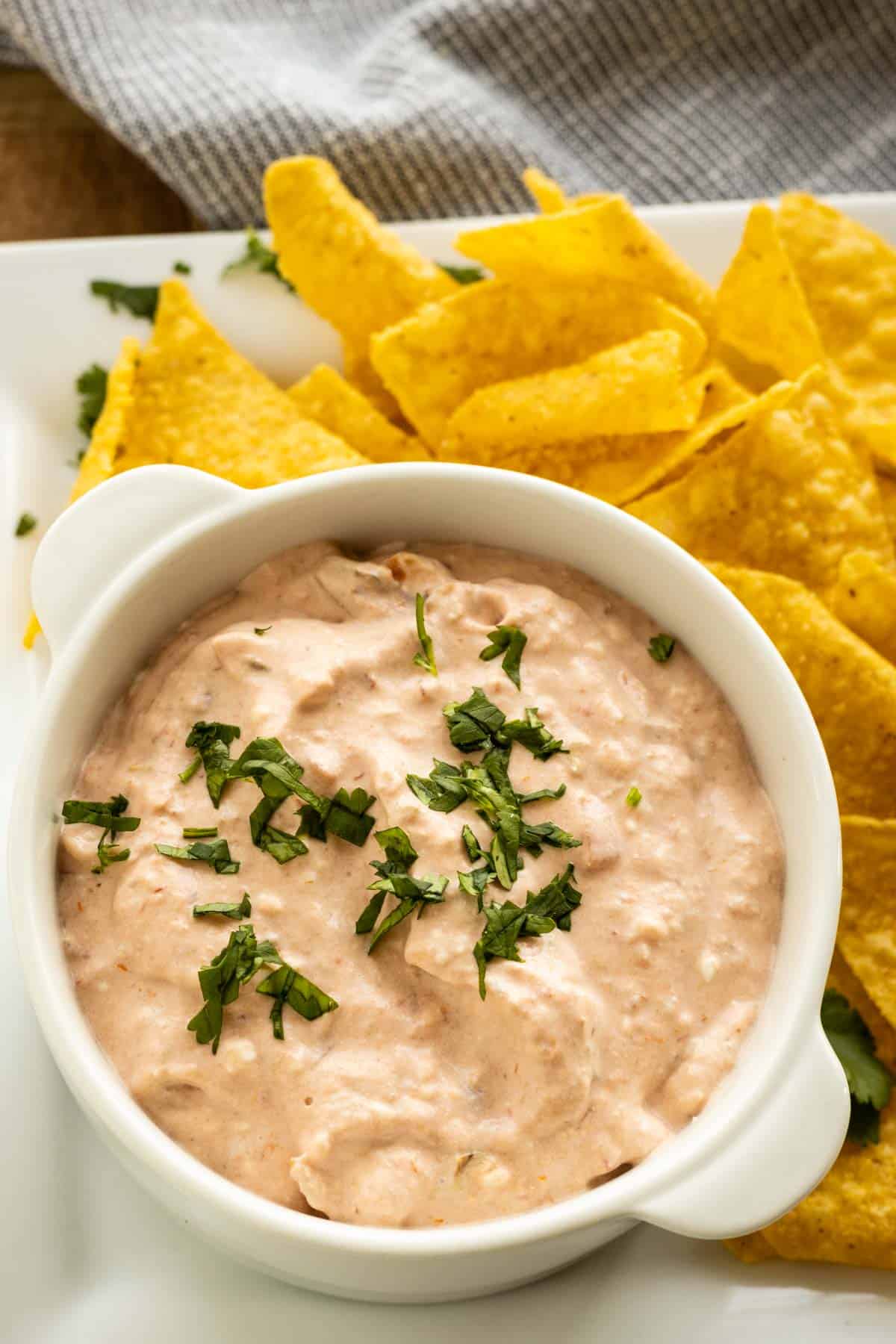 A white dish with cream cheese salsa dip topped with chopped cilantro and tortilla chips. 