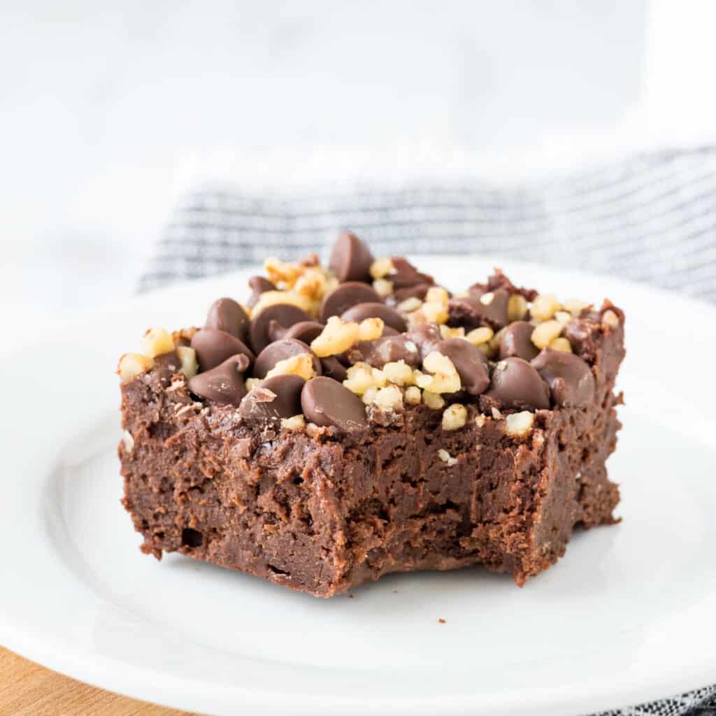 A brownie square topped with chocolate chips and walnuts on top with a bite out of it.