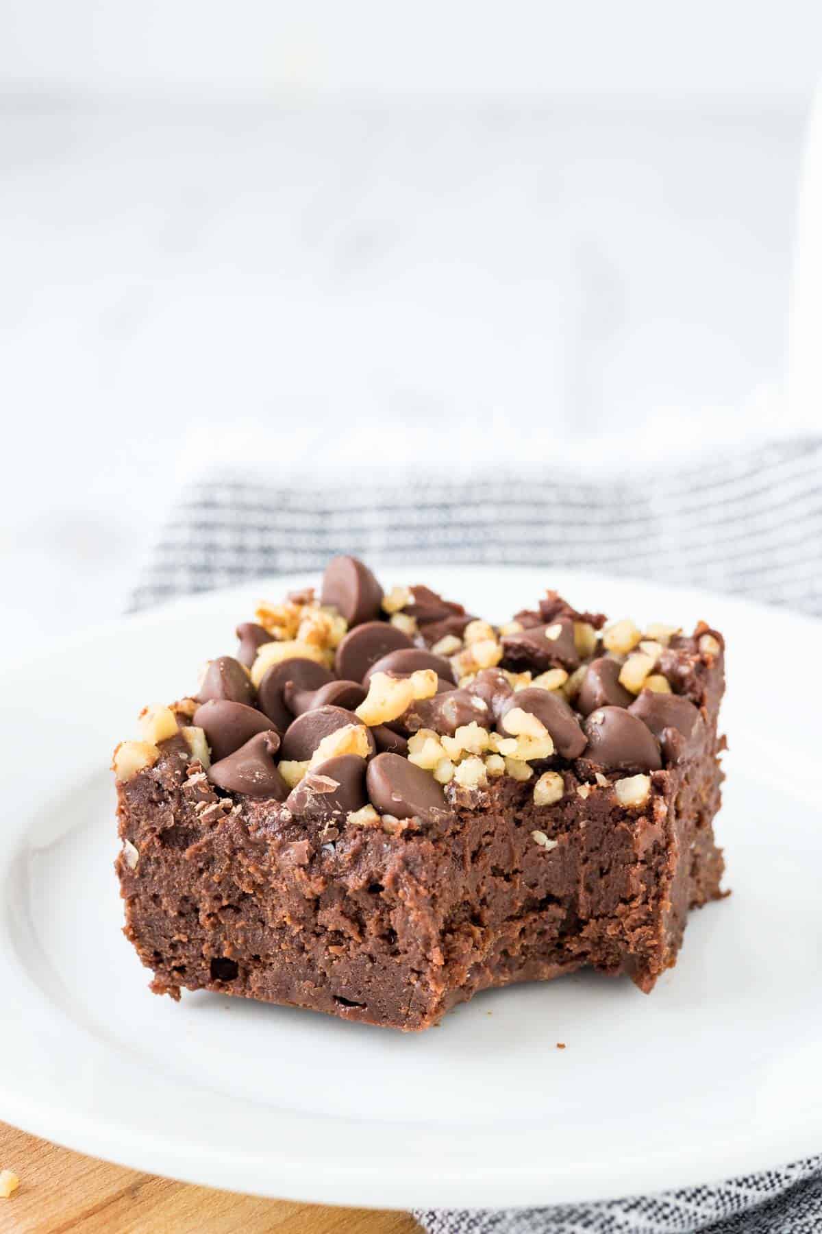 A brownie topped with walnuts and chocolate chips on a white plate.