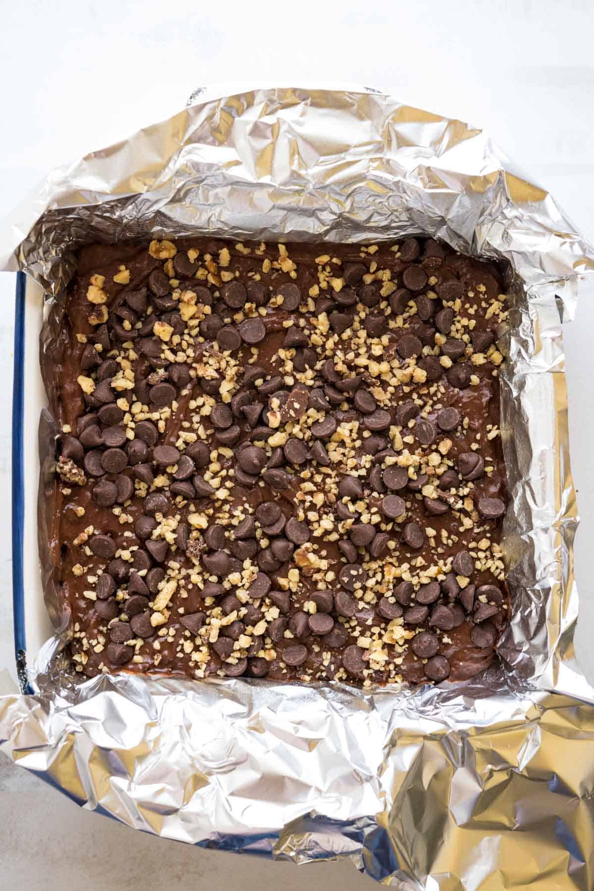 Brownie batter topped with chocolate chips and walnuts in a lined baking dish.