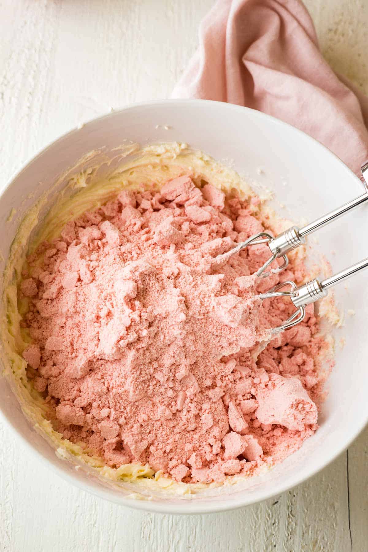 A strawberry cake mix dumped in a mixing bowl with electric beaters.