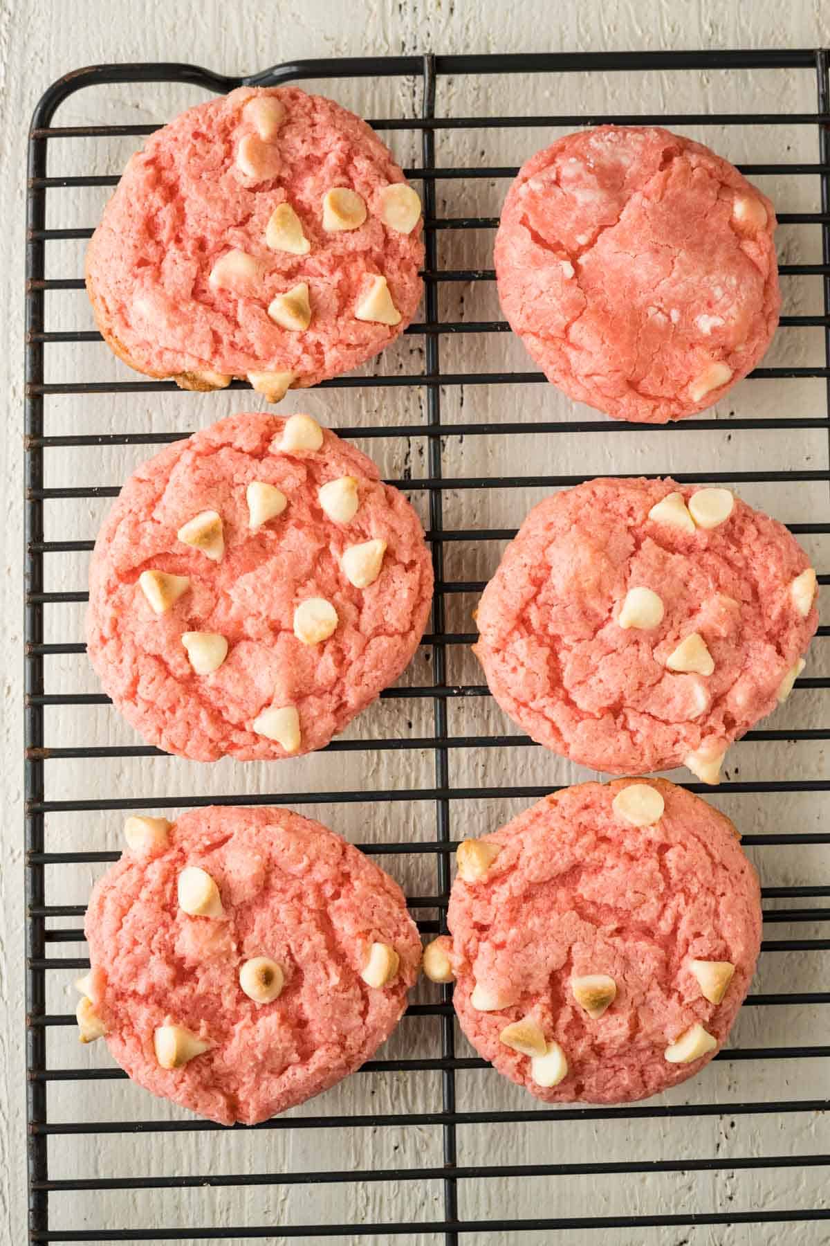 Baked strawberry cookies with white chocolate chips on a cooling rack.