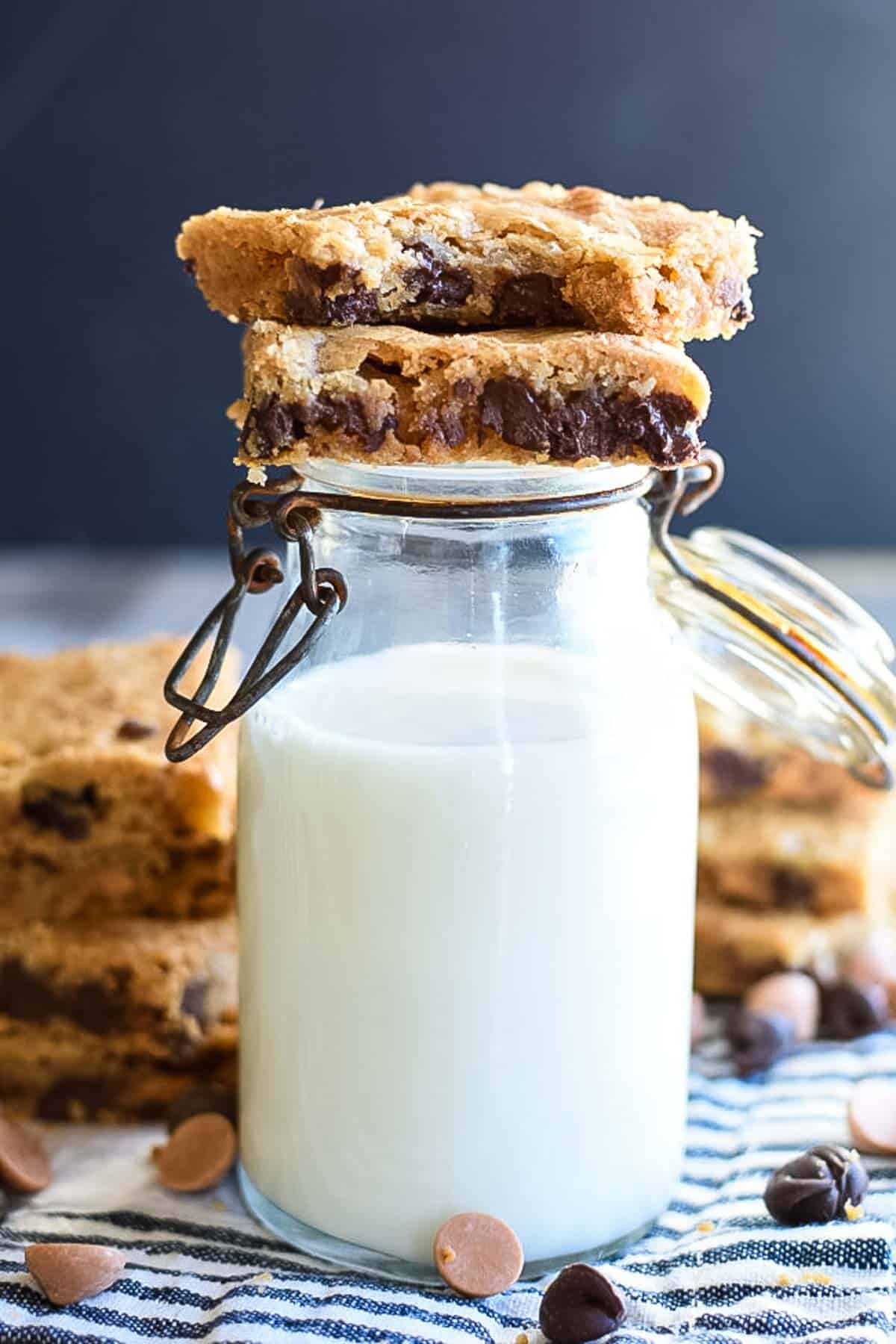 A jar of milk with two bar cookies sitting on top of it.