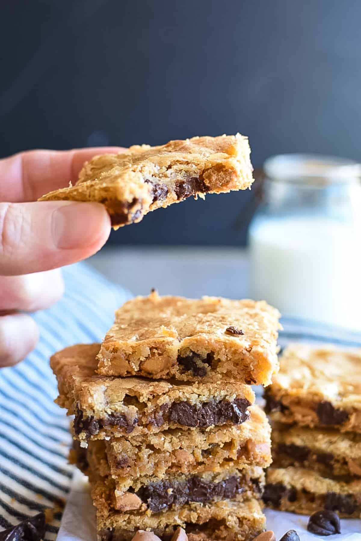 A butterscotch bar cookies with a bite being held over a stack of cookie bars.