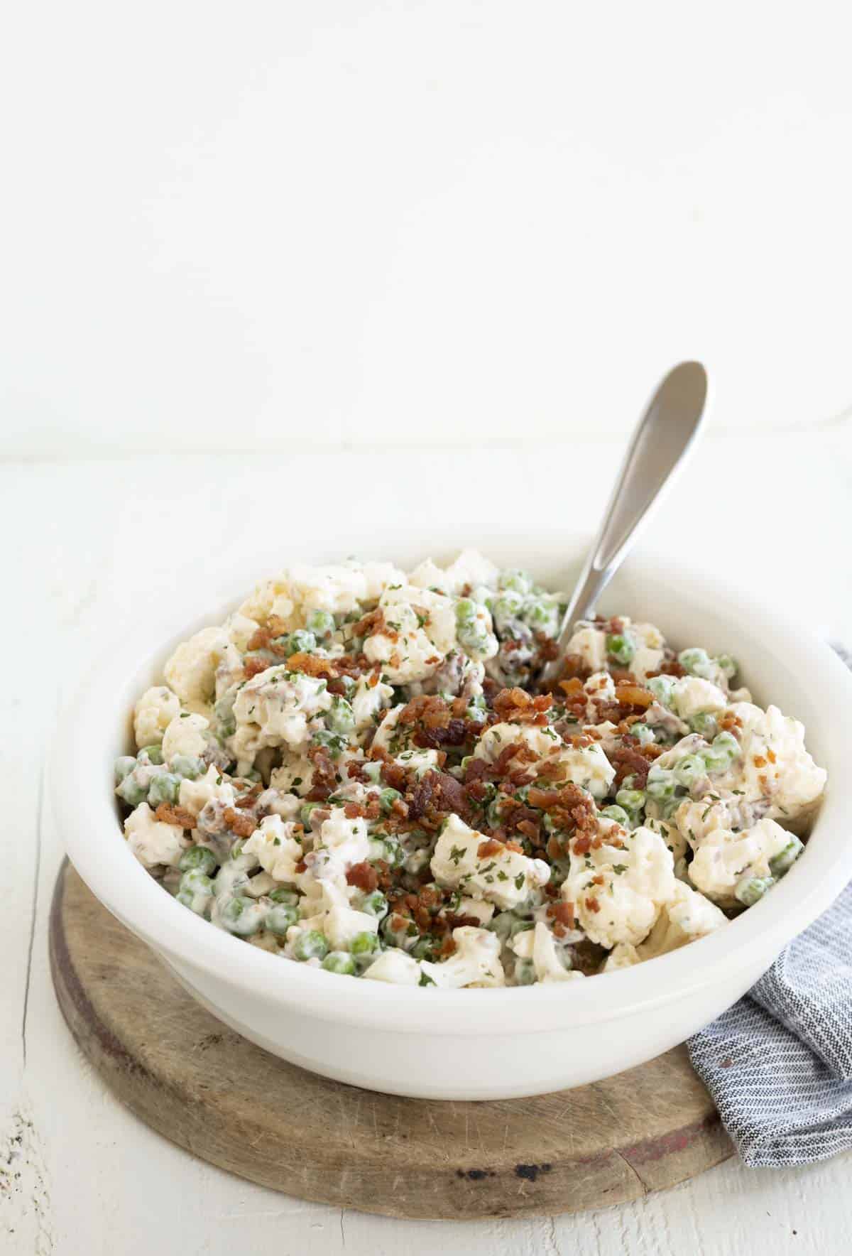 A bowl of cauliflower salad with peas and bacon.