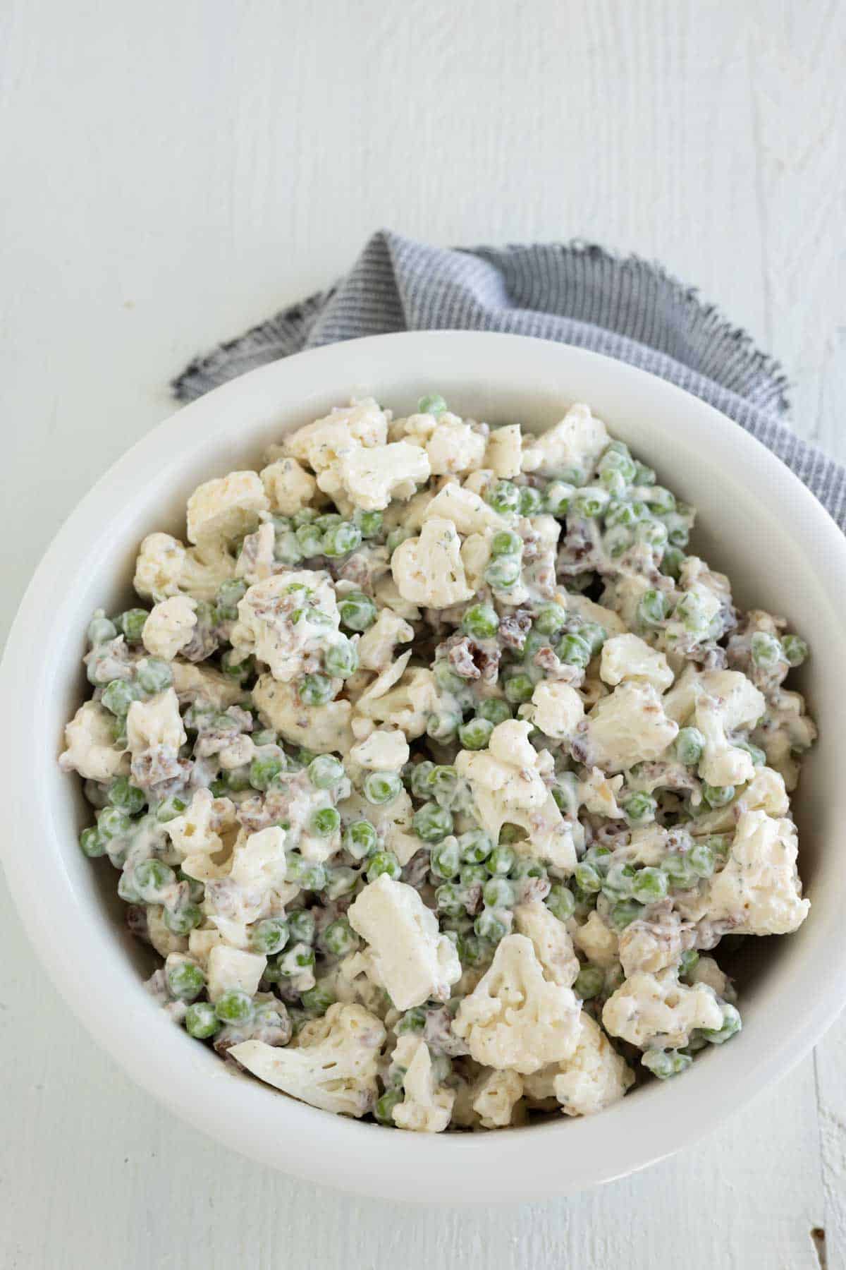 Pea and raw cauliflower salad with bacon and ranch dressing sprinkled with dill week herb.