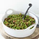 Green peas with bacon pieces in a white serving dish with a spoon.