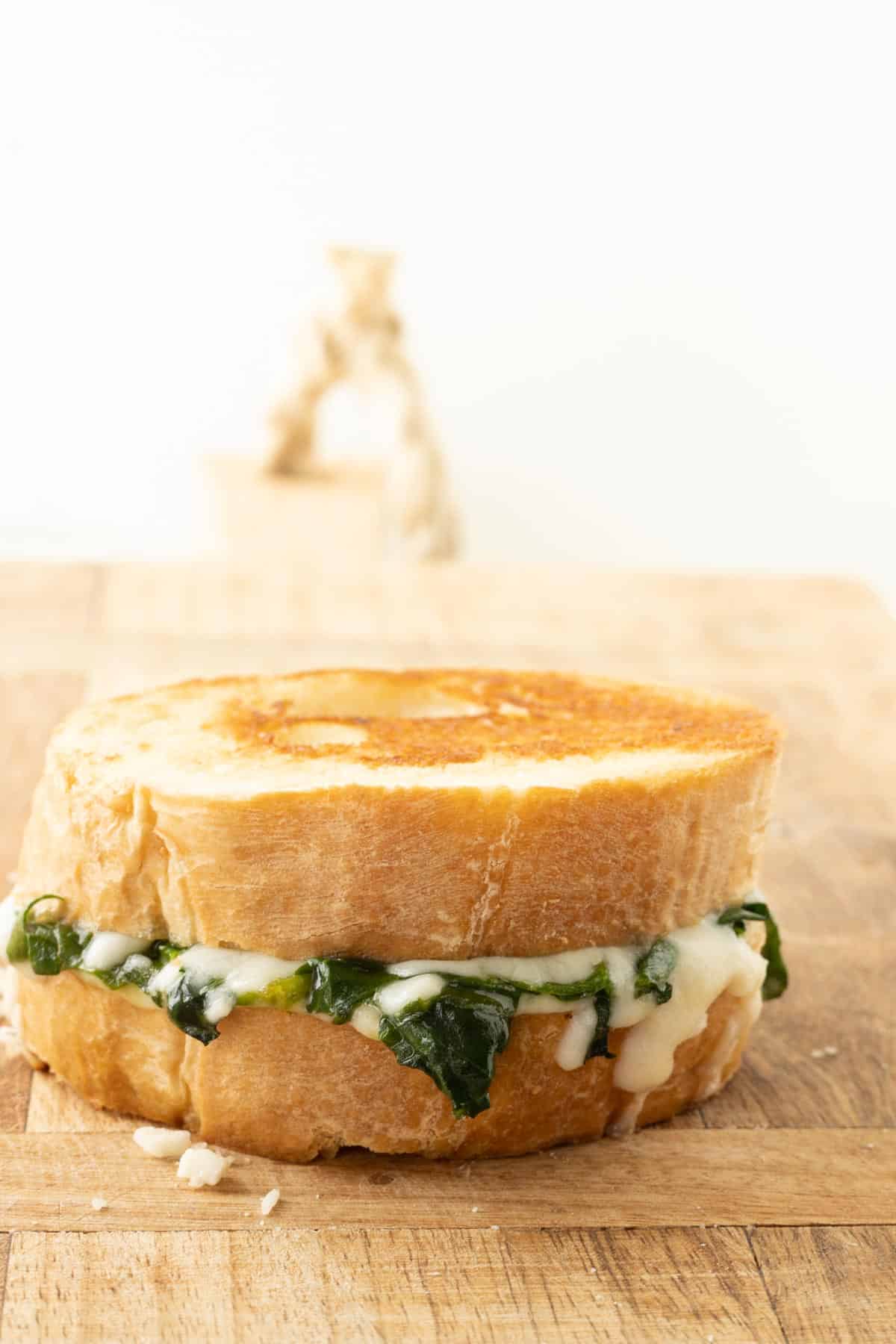 A toasted spinach and cheese sandwich on a wooden cutting board