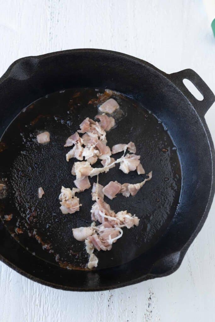 Pieces of raw bacon in a cast iron skillet.