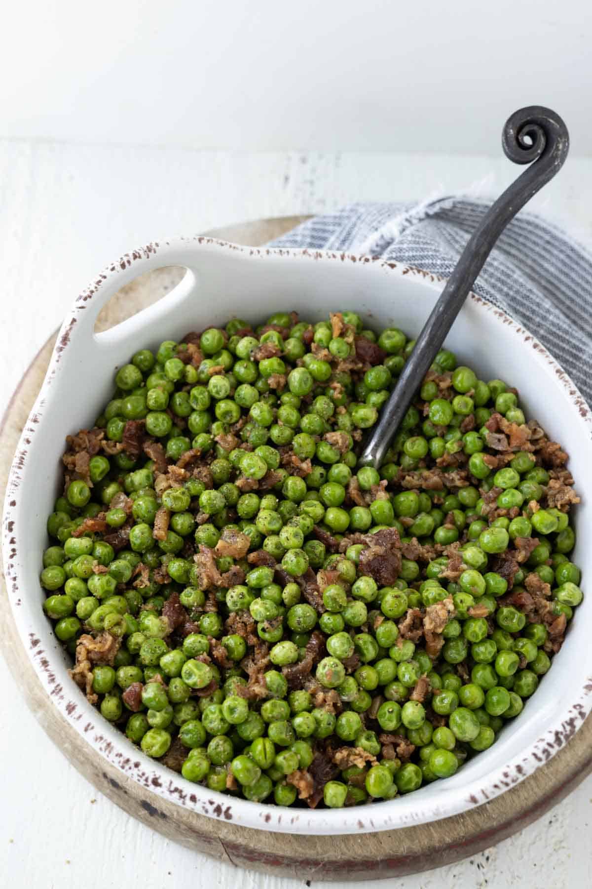 Green pea and bacon side dish in a white serving dish.