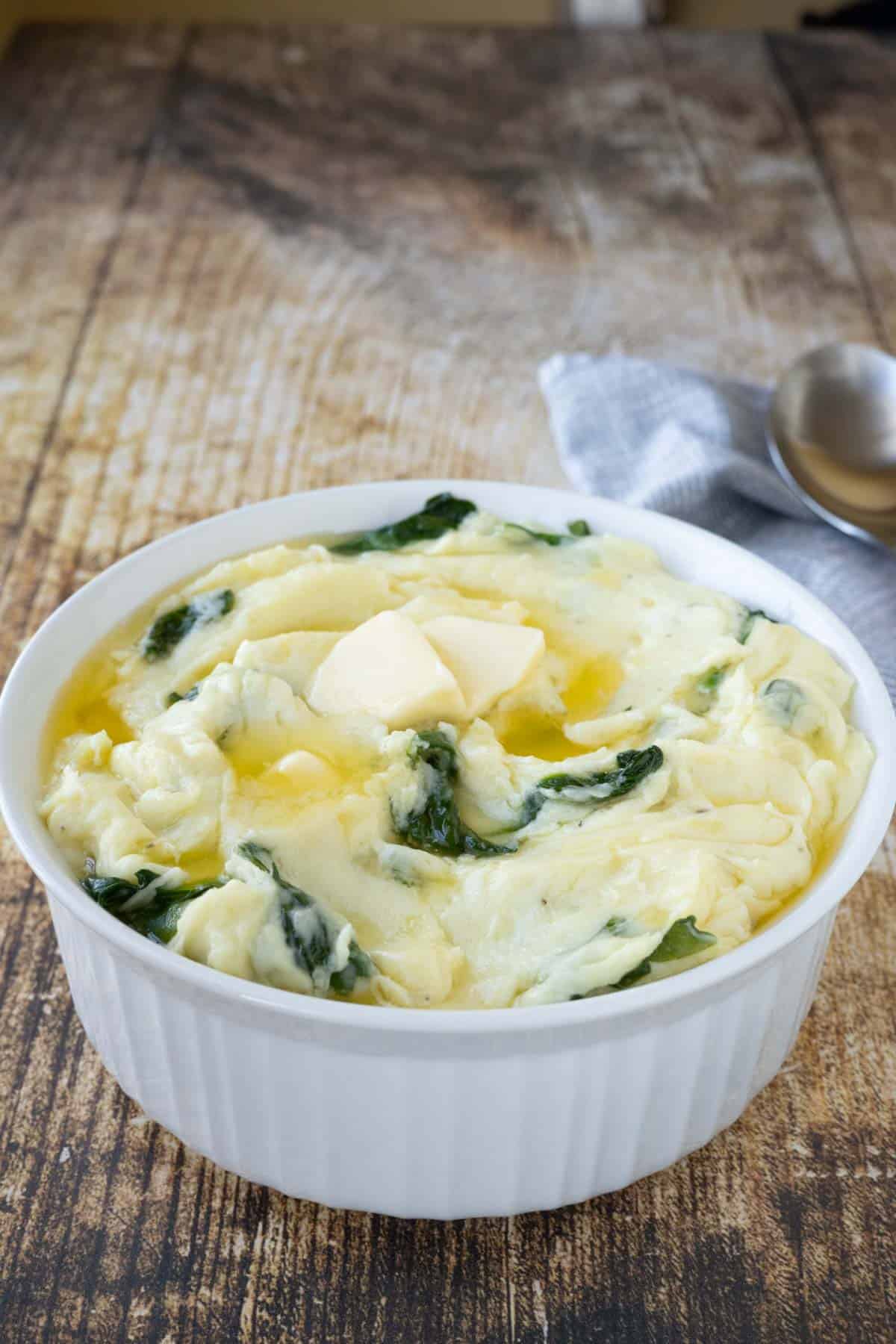 A serving dish with mashed potatoes and spinach with melted butter on top.
