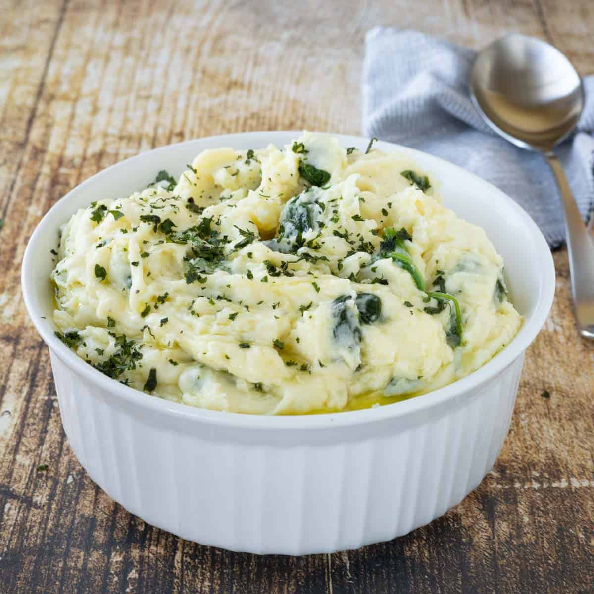 A white bowl with mashed potatoes with spinach and fresh parsley on top.