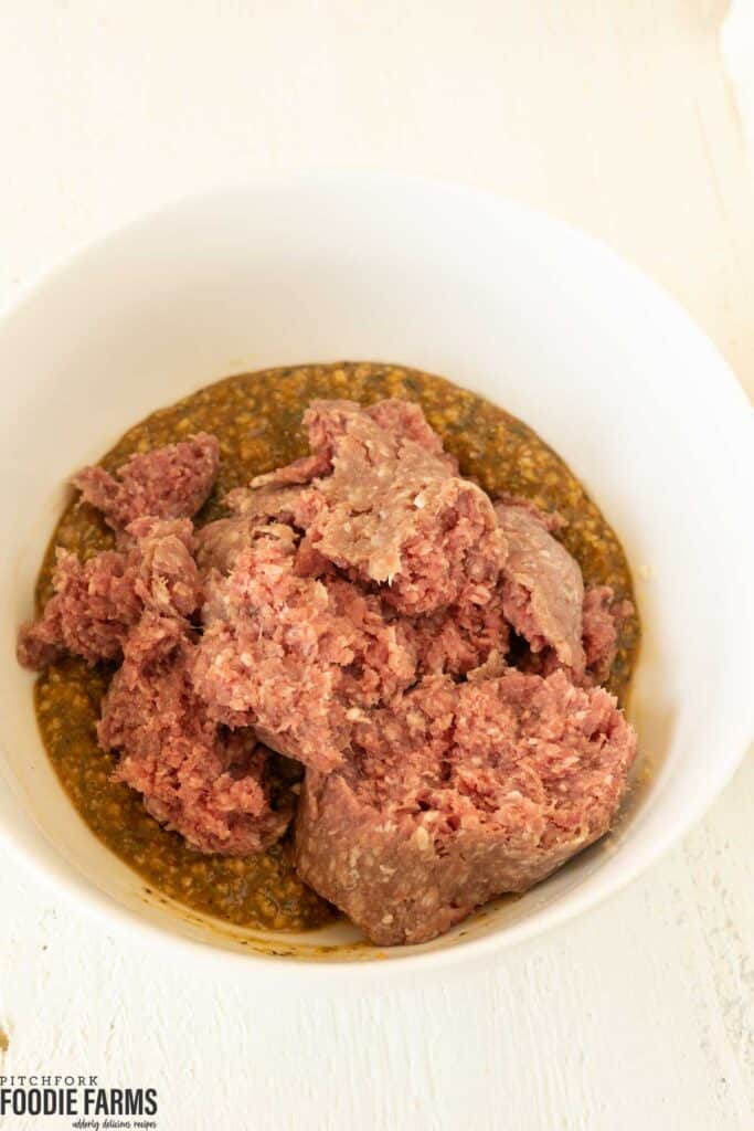 Ground beef in a mixing bowl with other ingredients to make meatloaf.