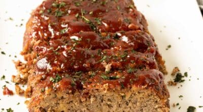 Smoked meatloaf cut into slices and set on a white plate.