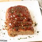 Sliced smoked meatloaf with a bbq glaze and chopped parsley on top.