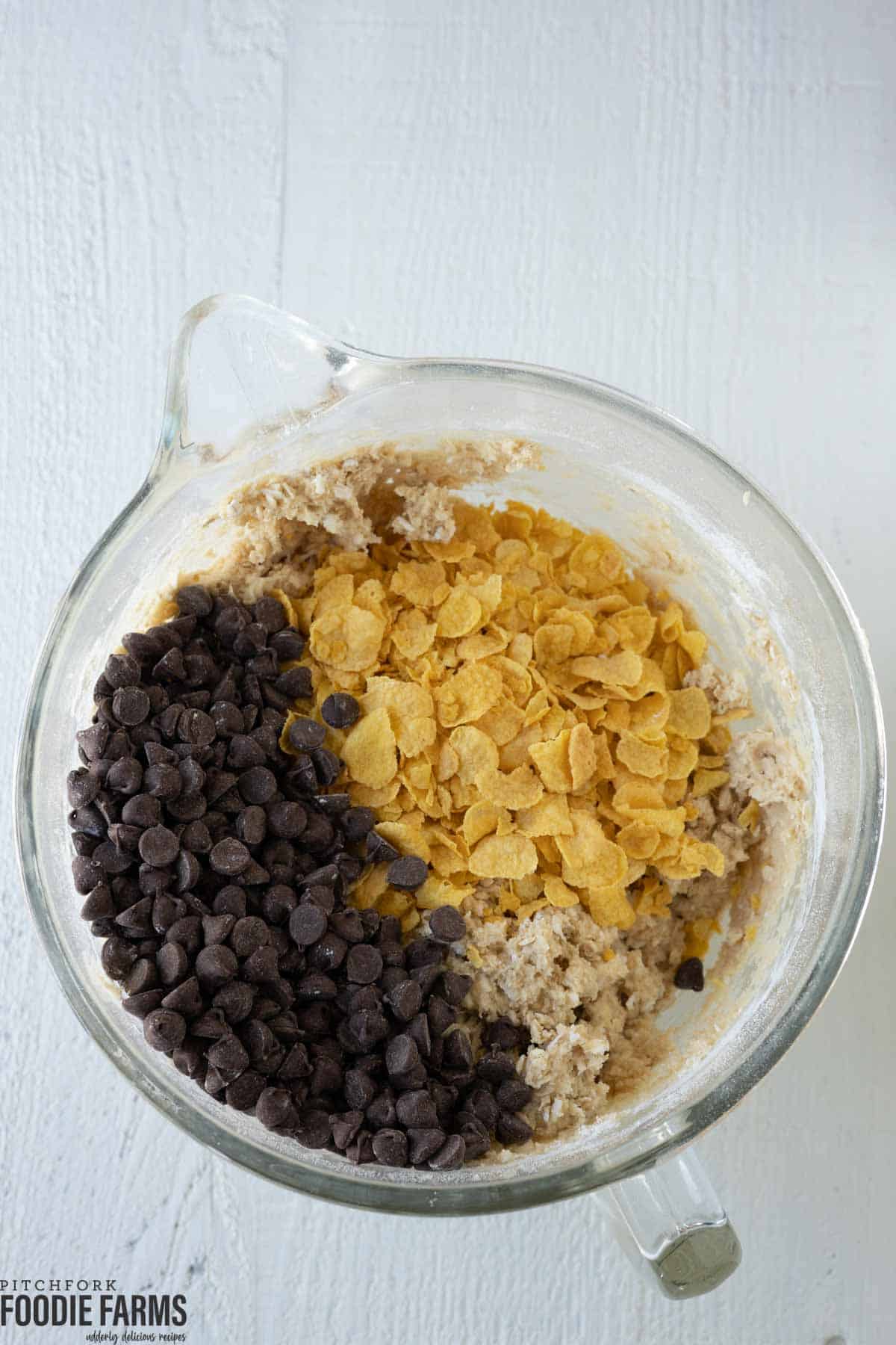 A mixing bowl with cookie dough and corn flakes and chocolate chips on top.