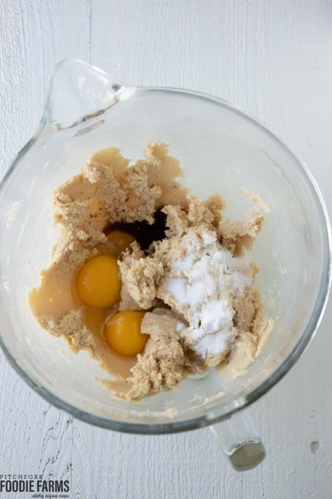 Creamed butter and sugar in a mixing bowl with eggs, vanilla, baking soda, salt, and baking powder on top.