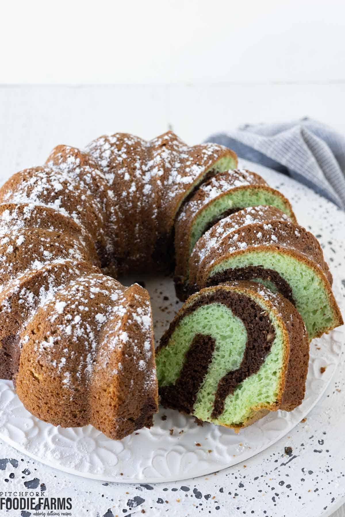 A chocolate pistachio marbled bundt cake with a few slices of cake on a plate.