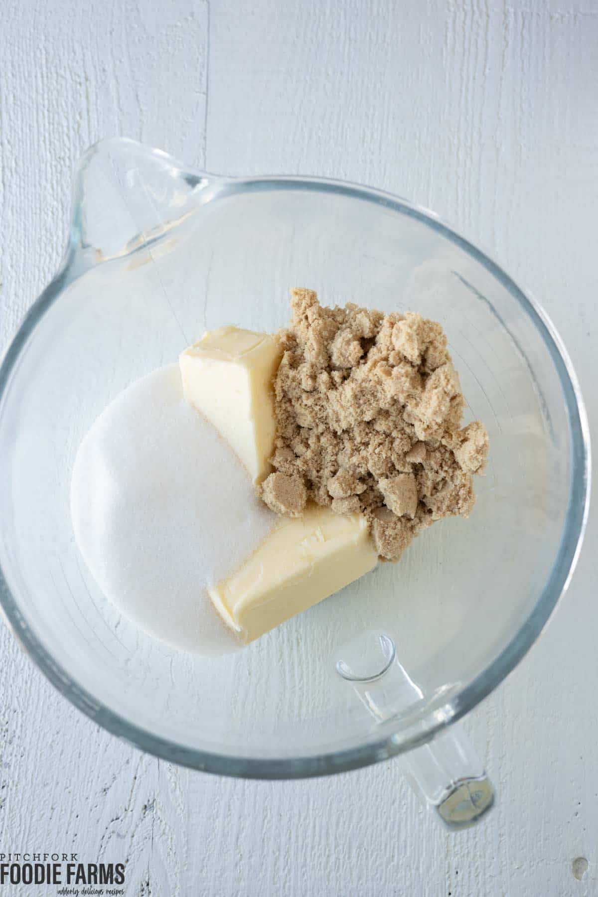 Two sticks of butter, granulated sugar, and brown sugar in a mixing bowl.