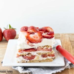 A square of strawberry icebox cake with layers of graham crackers, cream cheese filling, and sliced strawberries on a white plate.