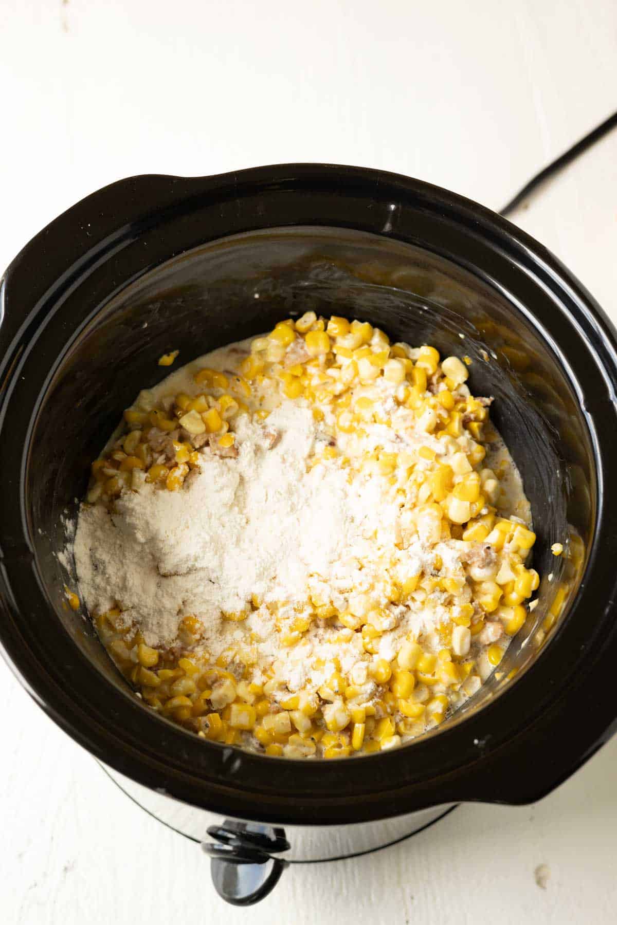 Cheesy corn in a slow cooker with flour sprinkled over the top.