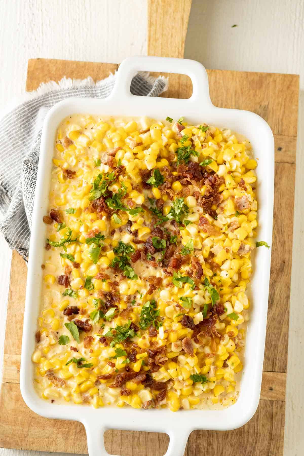 Cheesy corn casserole topped with crumbled bacon and parsley in a baking dish.