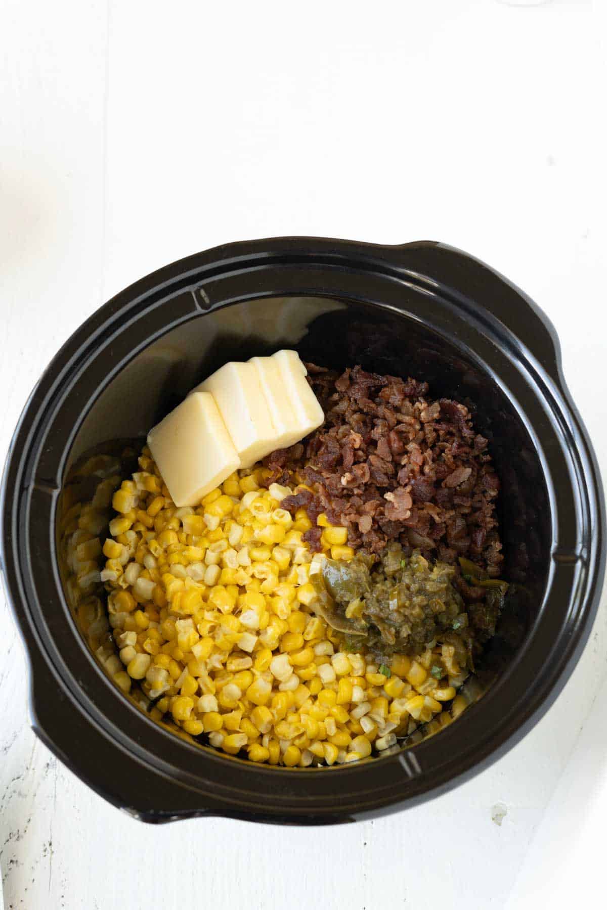 Corn kernels, crumbled bacon, diced jalapenos, and butter in a slow cooker.