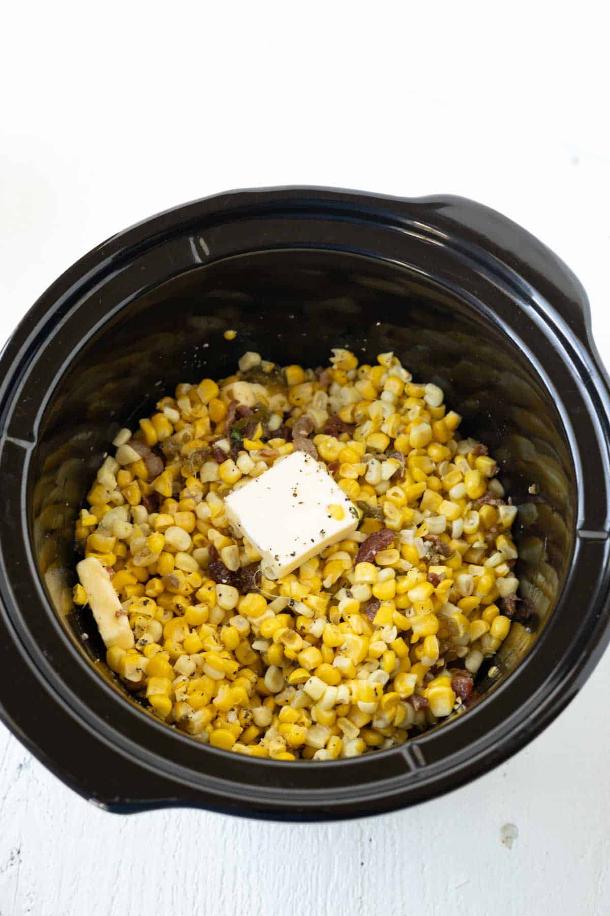 Corn casserole with bacon in a crock pot with slices of butter.