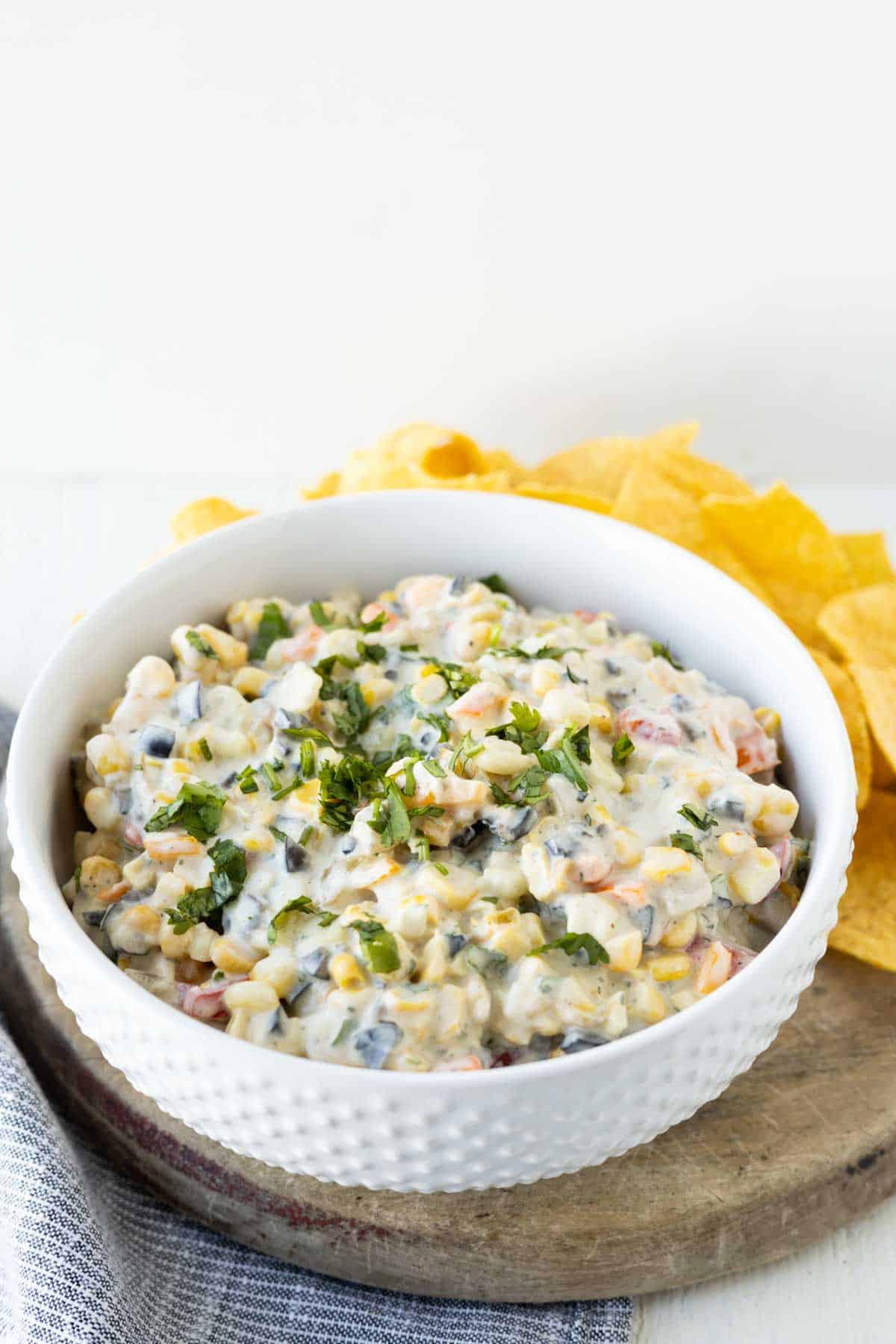 Image of poolside cream cheese dip with corn, peppers, olives, and herbs with tortilla chips.