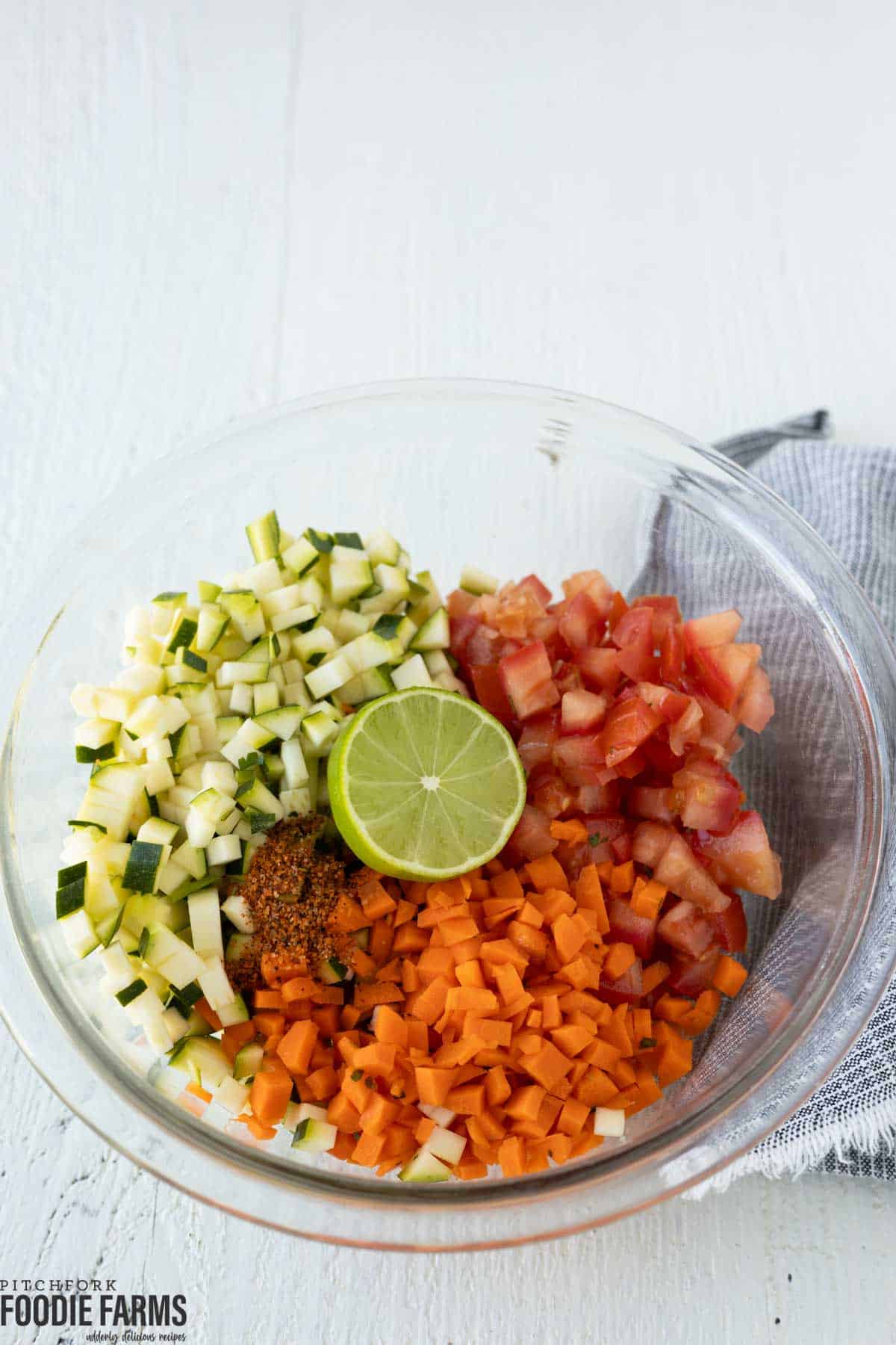 A bowl with diced zucchini, carrots, tomatoes, and half of a lime.