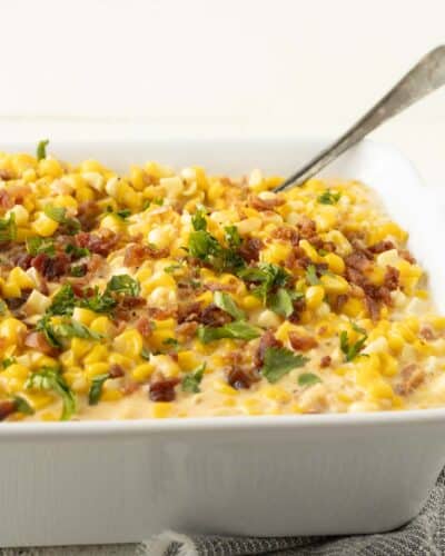 A dish of cheesy and cream corn with bacon and parsley on top.