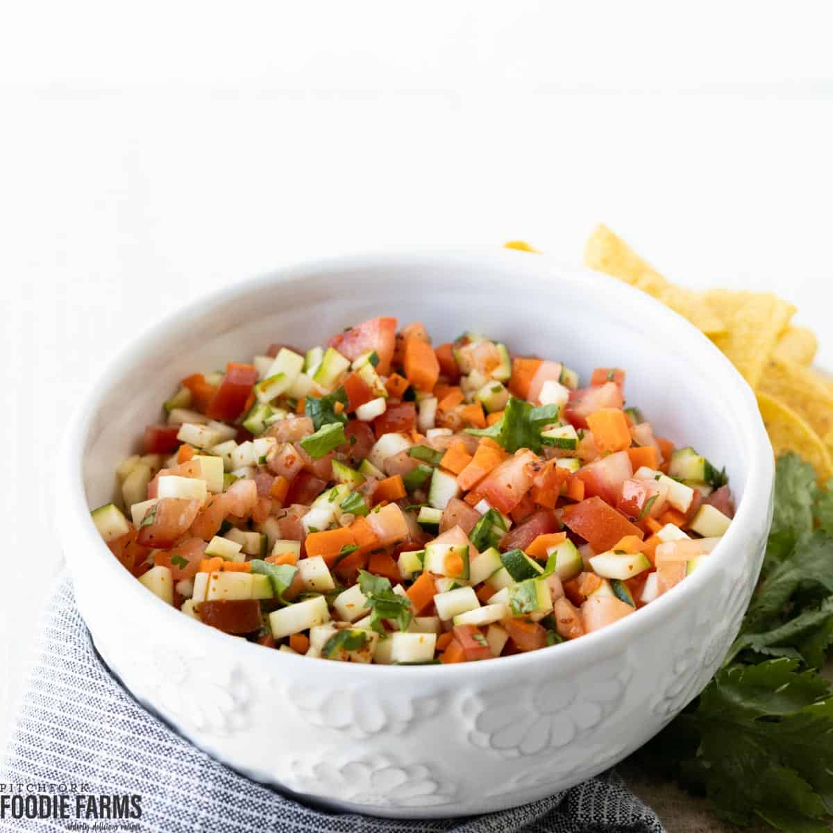 A white bowl with zucchini squash salsa and chips.