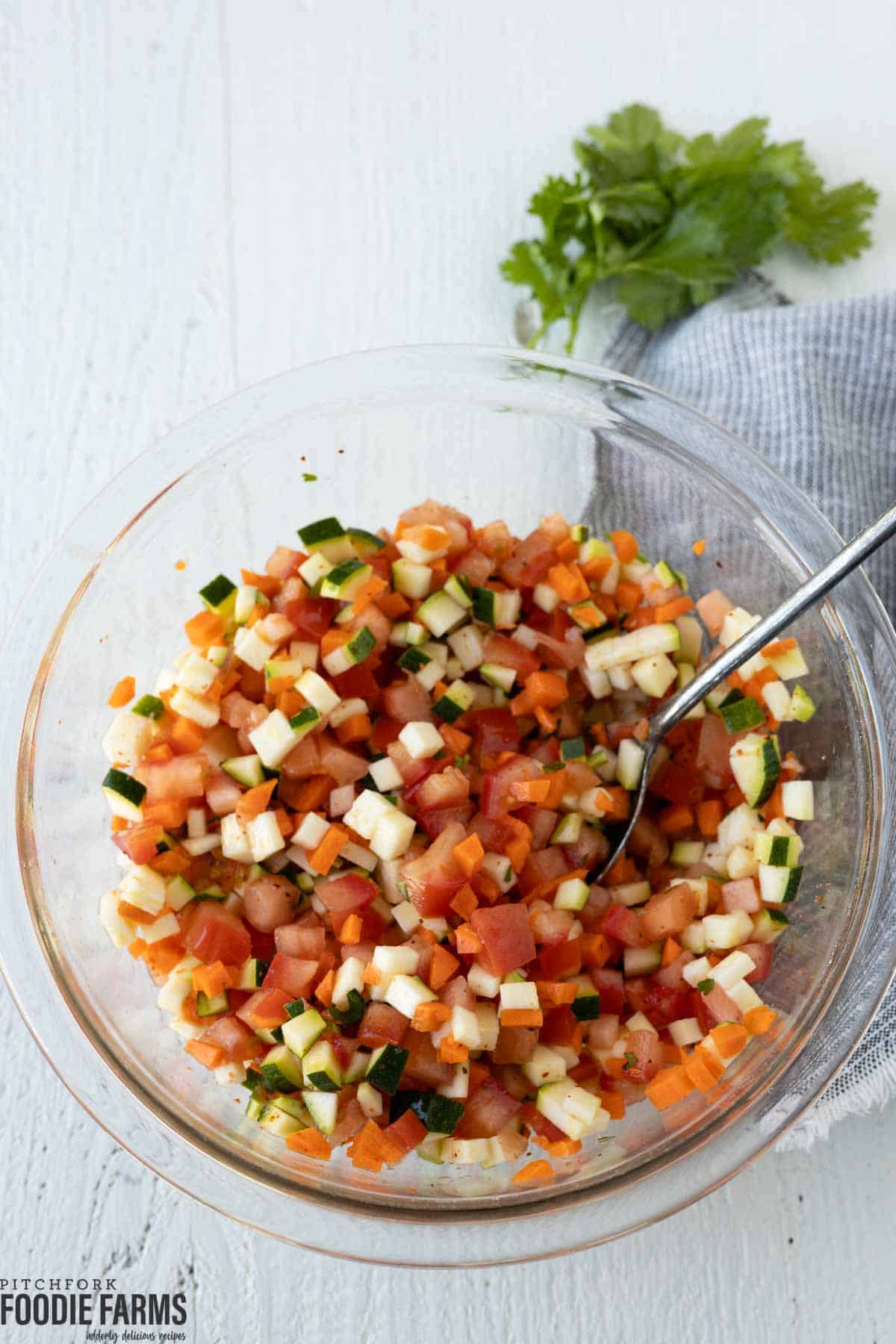 A glass bowl with diced raw veggies; carrots, zucchini, and tomatoes.