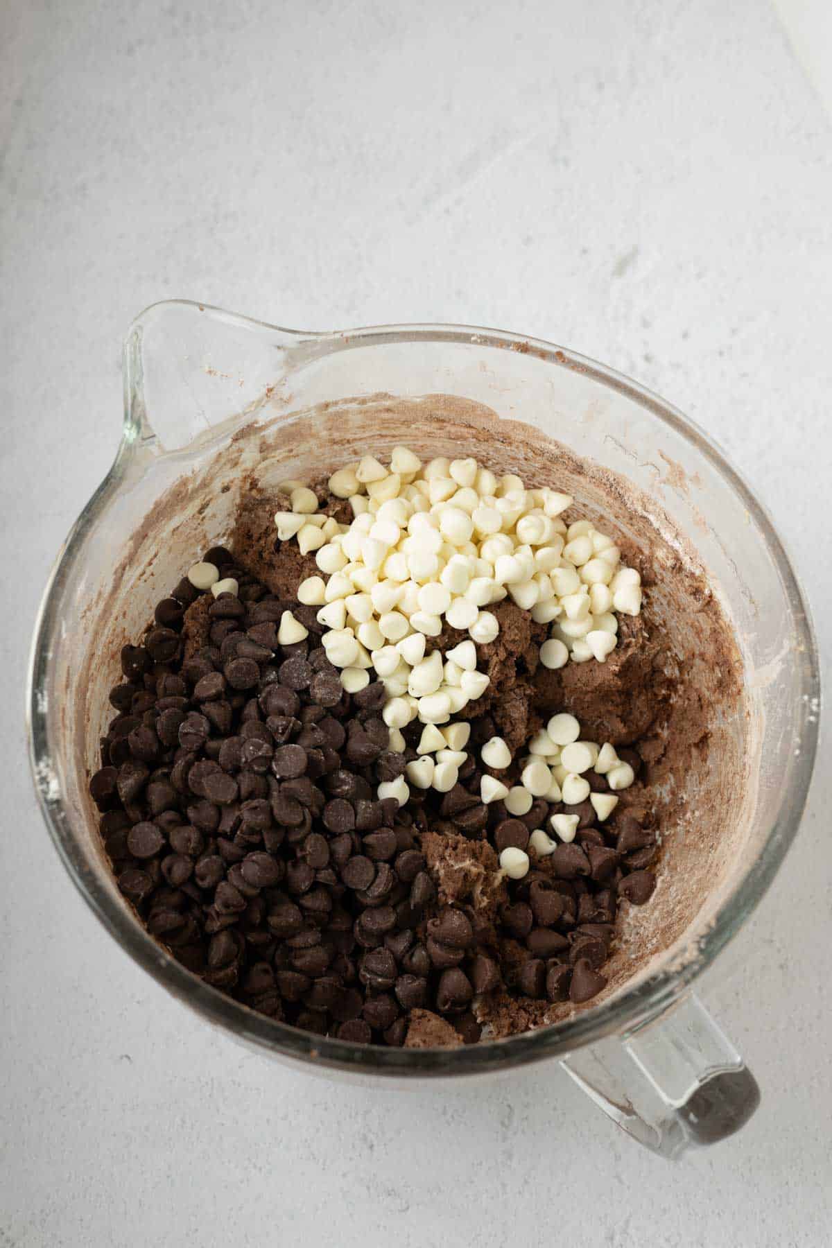 Chocolate cookie dough with milk chocolate, semi sweet chocolate and white chocolate chips in a mixing bowl.