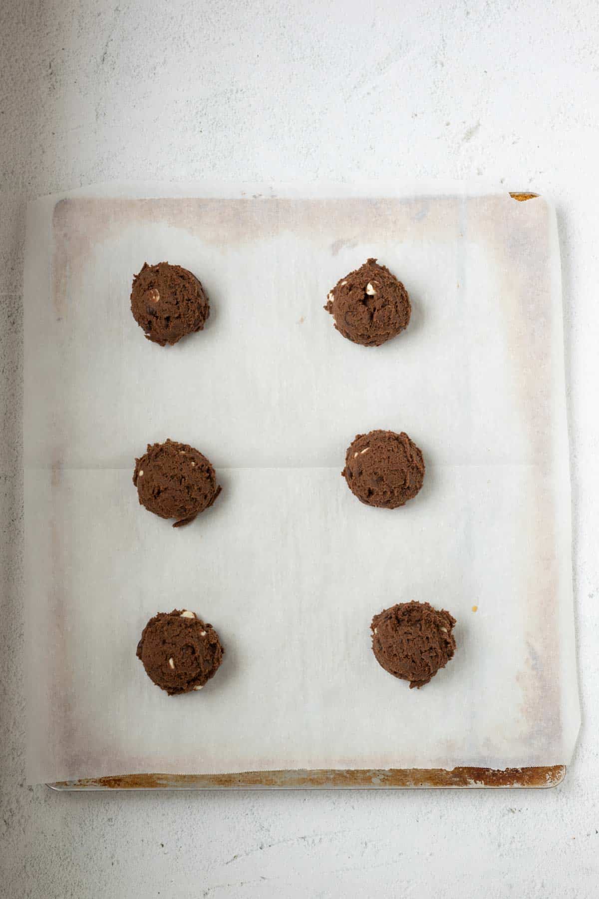 Chocolate cookie dough balls on a parchment paper lined cookie sheet.