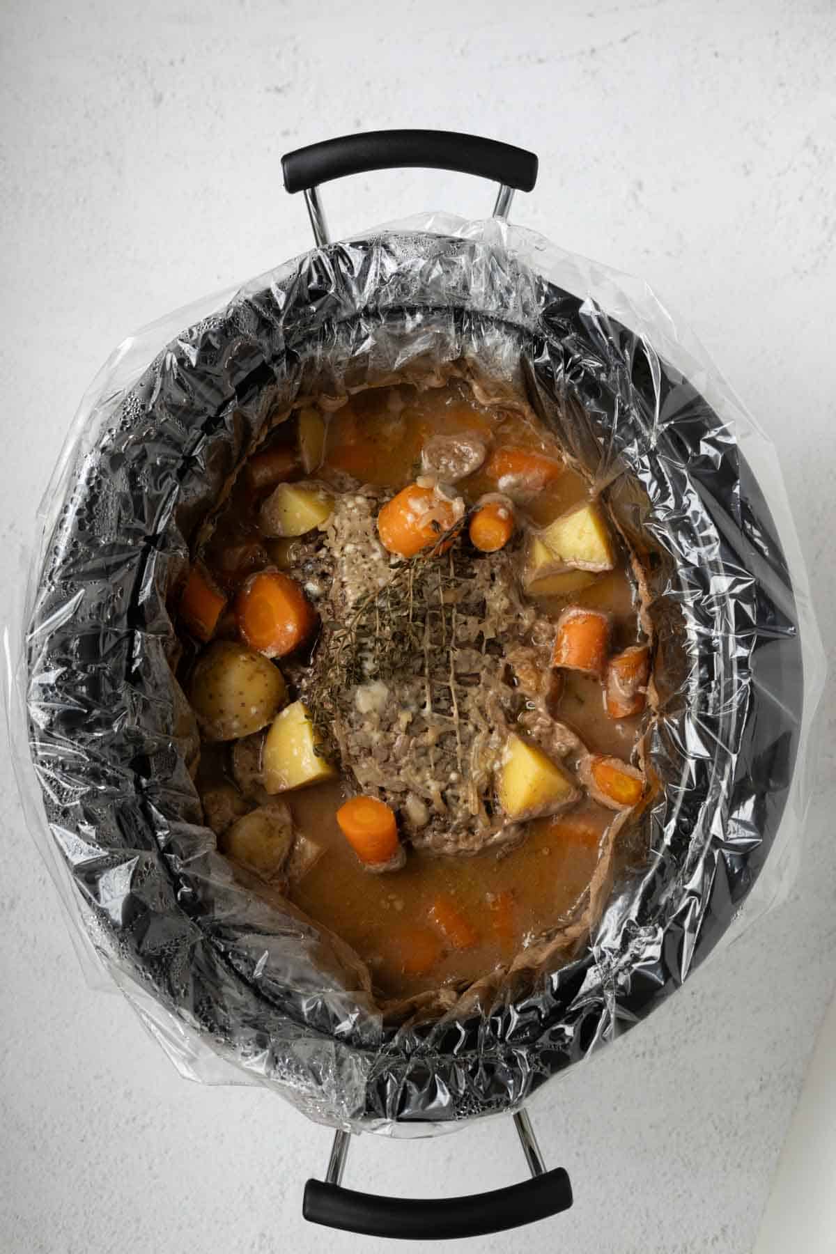 A cooked pot roast with vegetables in a slow cooker.