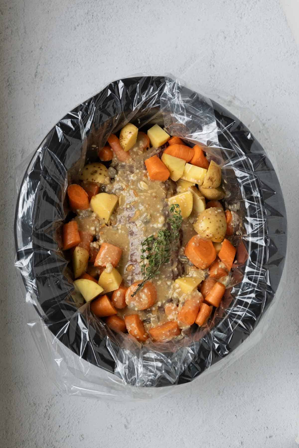 A slow cooker with a roast, diced carrots, potatoes, and mushroom soup gravy.