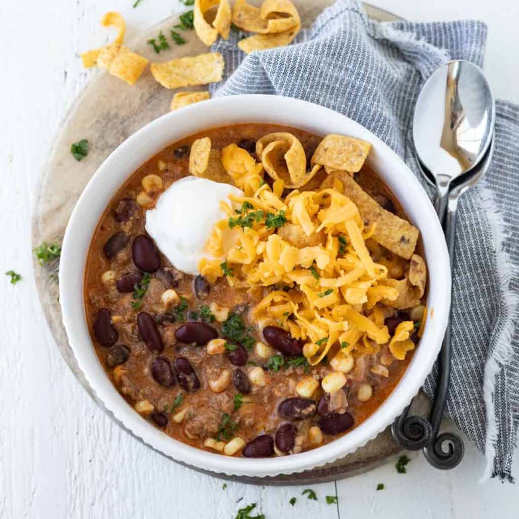 A bowl of creamy taco soup with cream cheese topped with grated cheese, corn chips, and sour cream.