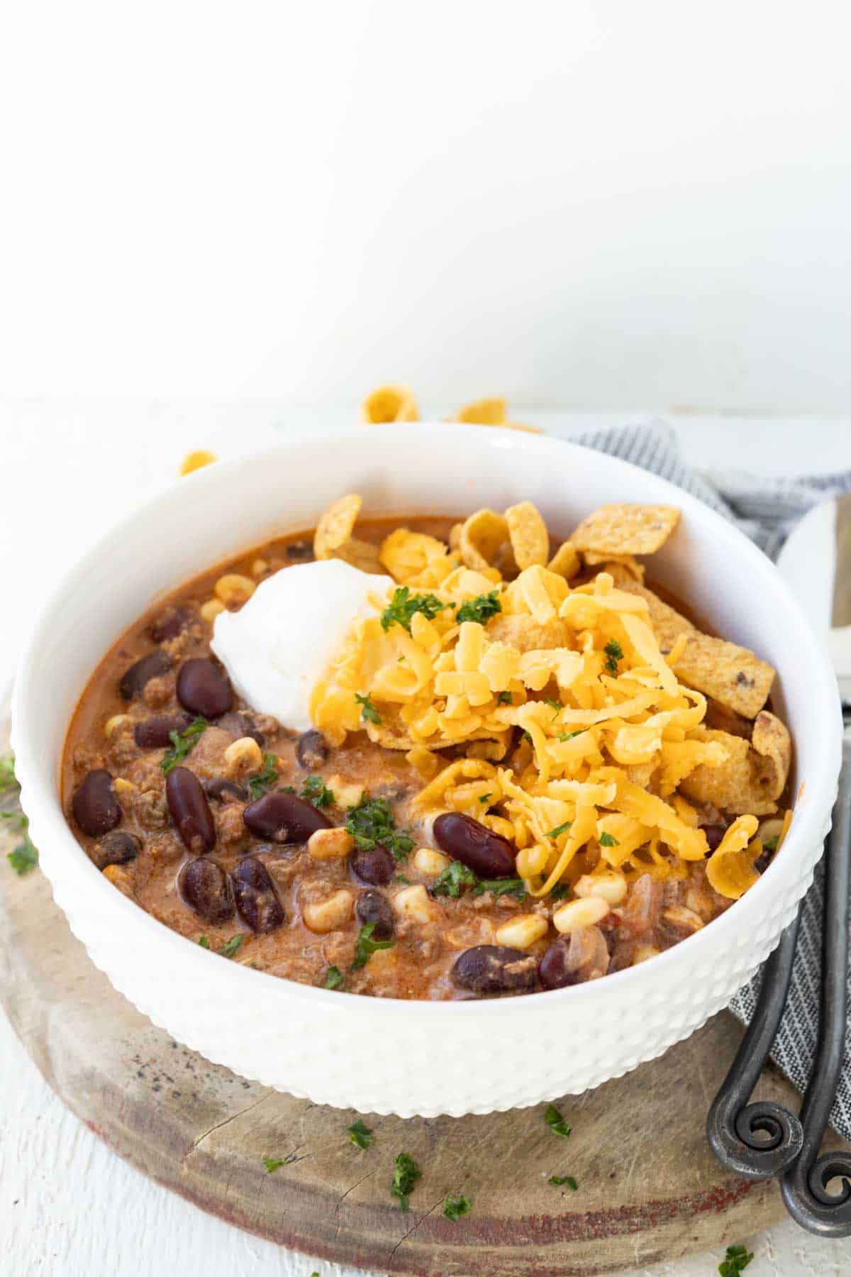 Creamy ground beef taco soup with kidney beans, corn, and black beans topped with corn chips and grated cheese.