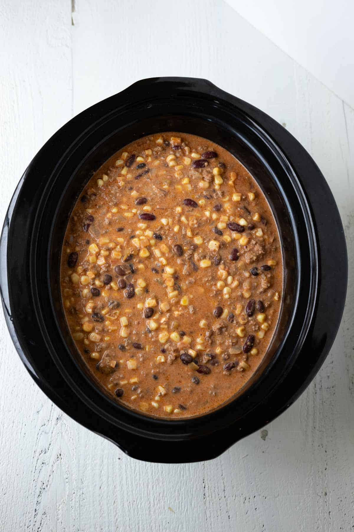 Creamy beef taco soup with black beans, corn, and ground beef in a slow cooker.